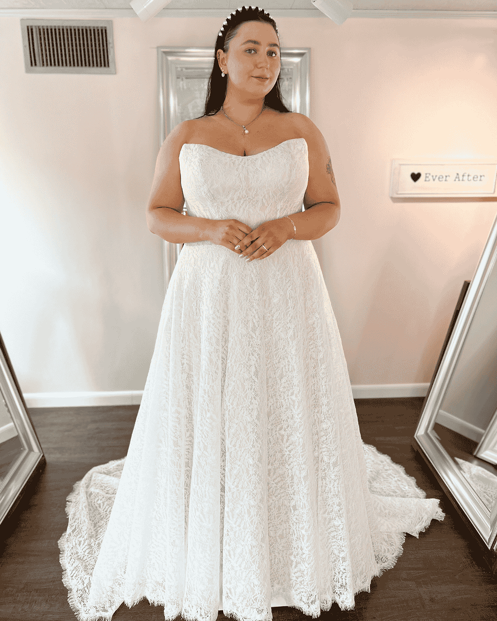 A bride in a white lace wedding dress with a fitted bodice and a flowing A-line silhouette, standing elegantly in a bridal shop.