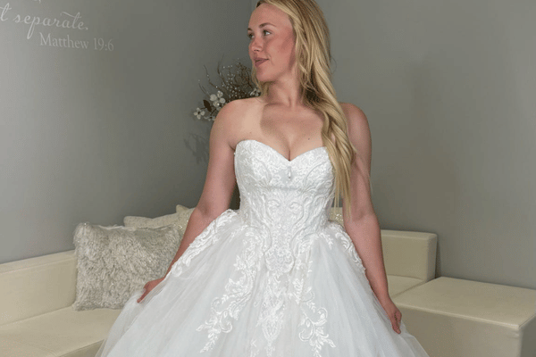 Blonde bride in a white strapless wedding dress stands by a cream sofa, with wall text reading separate Matthew 19:6.