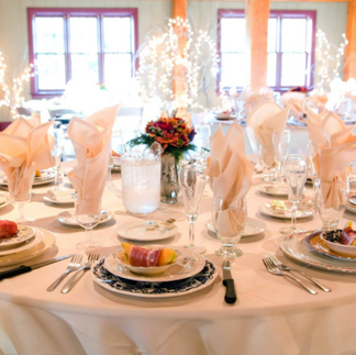 A beautifully set dining table with elegant plates, crystal glasses, and pink napkins, decorated with flowers.