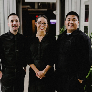 Three people in black outfits standing together in a bright hallway.