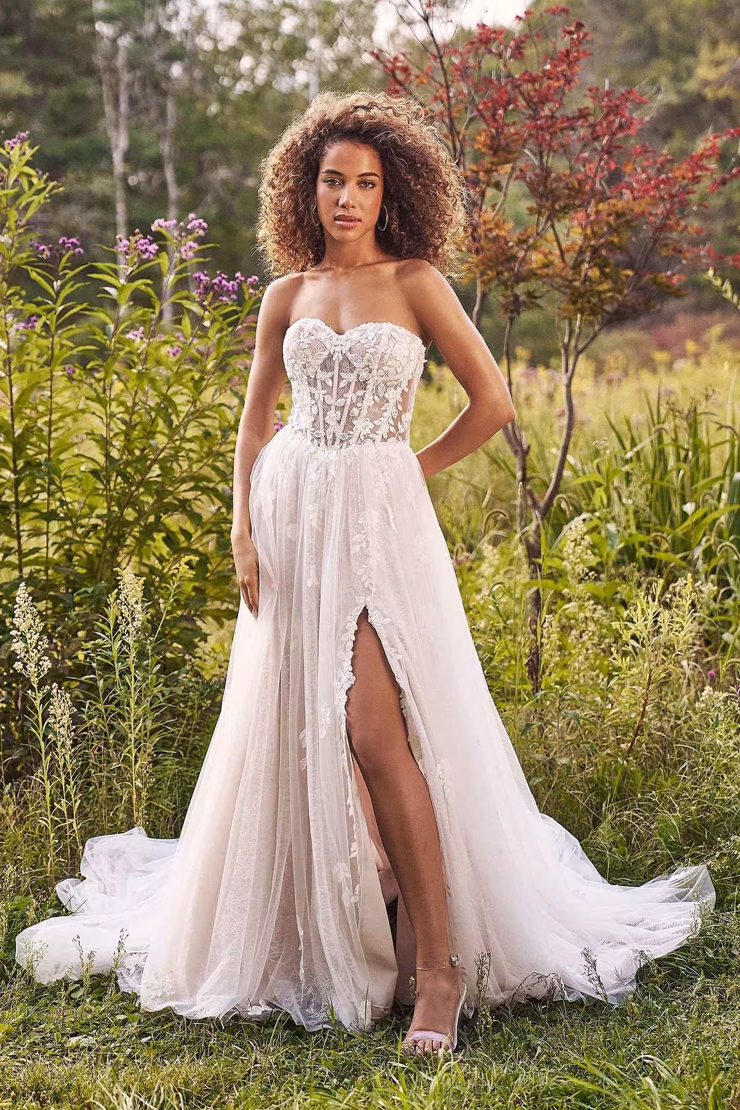 Bride wearing a Lillian West strapless lace A-line wedding gown with a front slit and flowing tulle skirt, photographed outdoors in a natural garden setting.