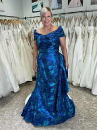 The mother of the bride in a sparkling teal gown stands on a pedestal