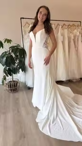 Bride wearing a Lillian West crepe wedding dress featuring a plunging V-neckline, illusion lace side panels, fitted silhouette, and a cathedral-length train with floral lace appliqués, posing at Blush & Ivory Bridal.