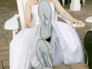 Bride in white dress lounges outdoors with feet up, showing Just Married on the soles of her shoes.