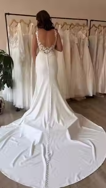 Back view of a bride wearing an Eddy K mermaid wedding dress featuring an illusion lace back, floral appliqué details, covered buttons, and a dramatic chapel-length train at Blush & Ivory Bridal.