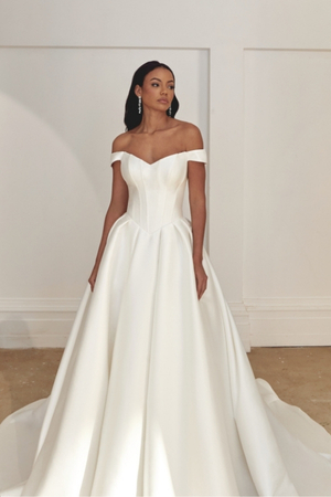 Bride wearing an off-the-shoulder satin ball gown wedding dress with a structured bodice and full skirt in a studio setting