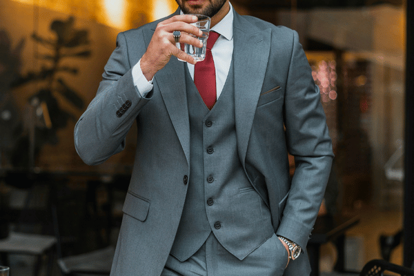 Man in a gray suit and red tie drinks water in a softly lit upscale bar or restaurant.