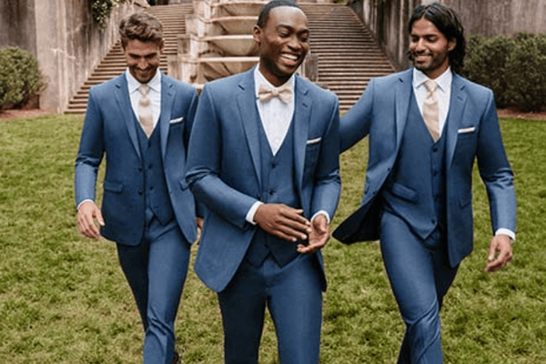 Three men in blue suits and light ties walk happily on grass, stairs in the background. Smiling, confident mood.