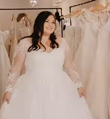 Bride wearing a long sleeve gown in front of a rack of bridal gowns.avif