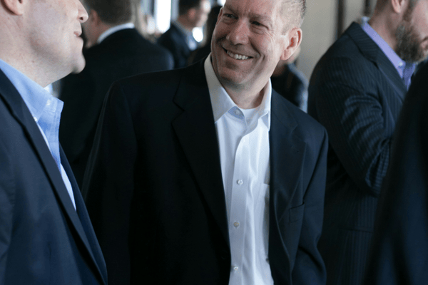 A group of men in suits are talking and smiling in a formal setting. The mood is friendly and engaging.