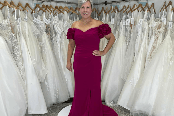 A woman in dark pink posing in front of a dress rack
