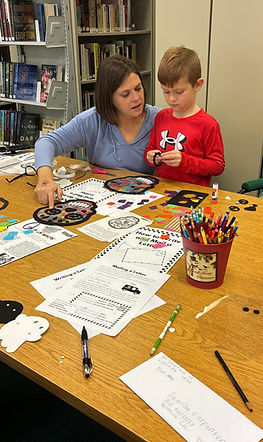 Woman and boy crafting at table with craft supplies in library.