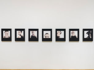 A series of nine framed black-and-white portraits displayed on a plain wall, showing various poses and expressions, conveying introspection.