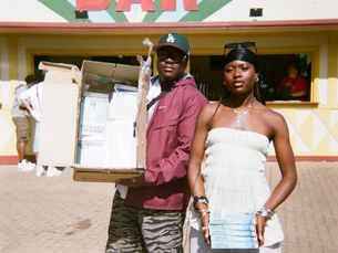 Two people smile beside a table full of books. Visible text emphasizes storytelling accessibility. Warm lighting.
