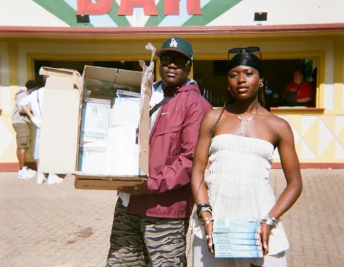 Two people smile beside a table full of books. Visible text emphasizes storytelling accessibility. Warm lighting.