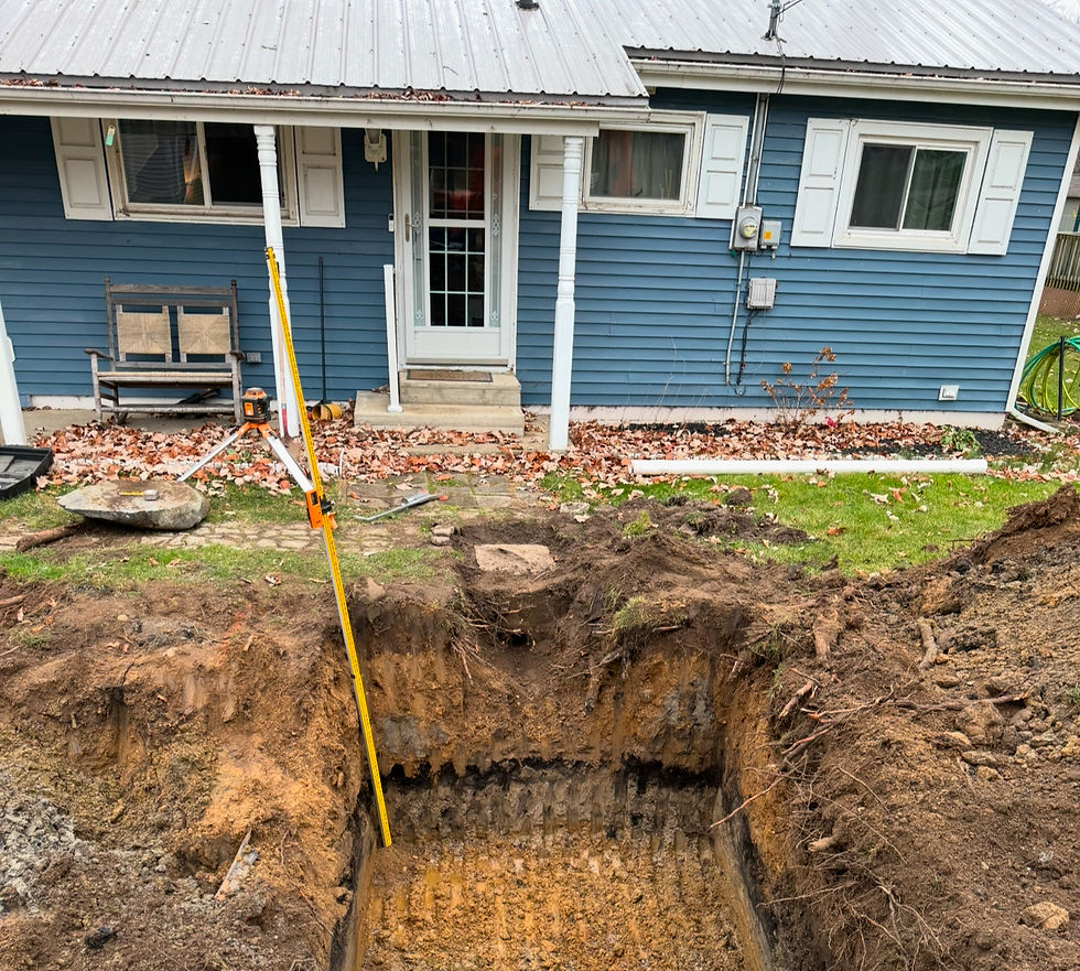 A deep pit dug in front of a blue house with white trim. A leveling tool stands upright. Fallen leaves cover the ground.