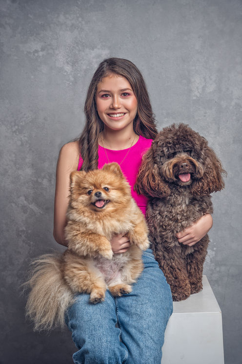 Quinceañera sonriente con sus dos perros frente a un fondo gris.