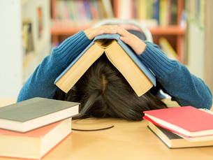 Học sinh úp sách lên đầu, ngồi gục trên bàn với nhiều sách vở xung quanh – hình ảnh minh họa stress học đường