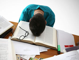 Học sinh gục đầu trên sách giữa bàn học nhiều tài liệu và sách vở, thể hiện sự mệt mỏi do áp lực học tập.