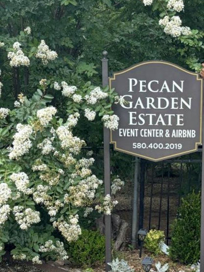 Pecan Garden Estate sign with text, surrounded by blooming flowers.