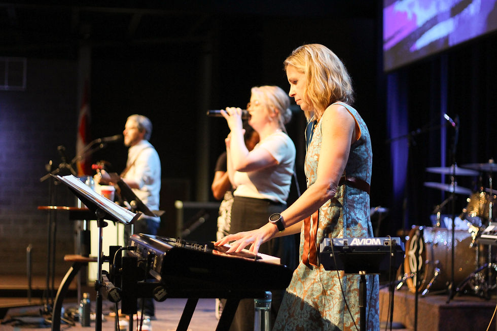 Woman playing the keyboard, woman singing, and man playing the guitar on stage