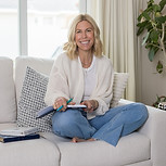 Steph Clymer Leader, Speaker and Business Coach sitting on couch smiling with her legs crossed and an open journal in her lap