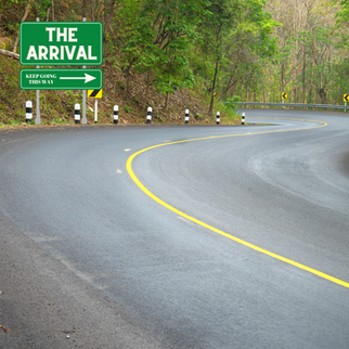 A curve along a tree lined road. A road sign is visible that says "The Arrival". There is a small sign beneath saying "Keep going this way". with a arrow pointing right
