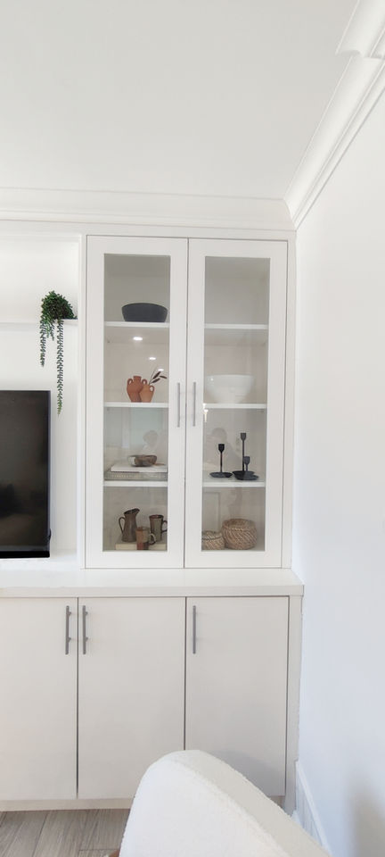 A custom built-in cabinetry unit in an open concept living room. Designed in a modern style using clean lines, this white painted wood cabinet has glass pane doors on top, making it functional while aesthetically pleasing.