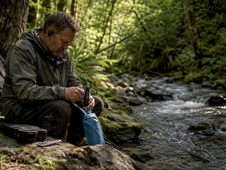 Man filtering water from mountain stream outdoors.