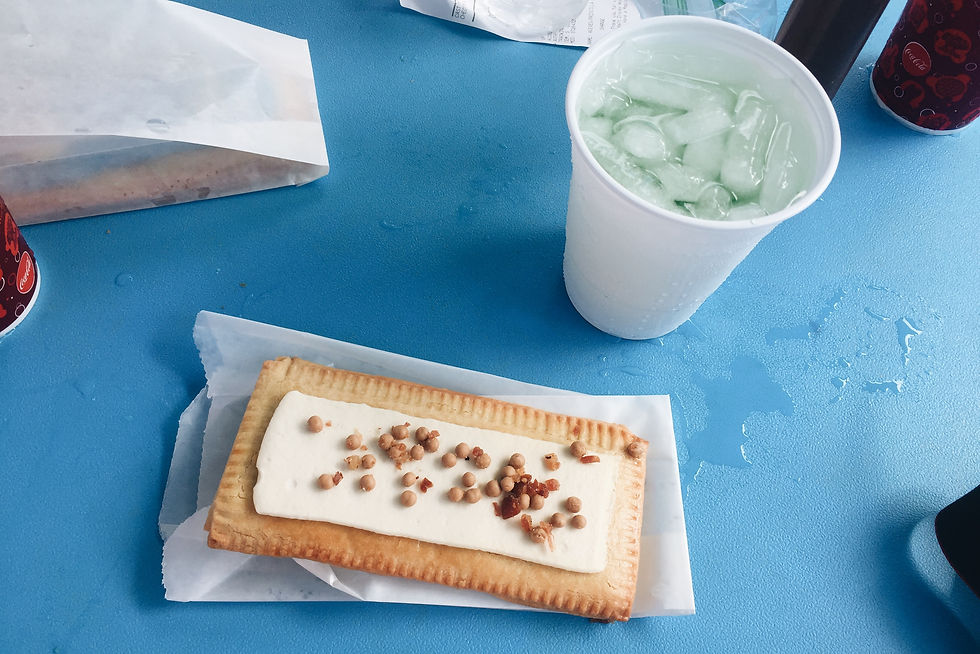 A snack tart with white frosting next to a cup of green punch with ice on a blue table.