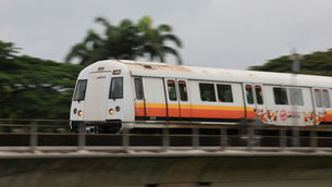 SMRT train travelling on an elevated track past tropical greenery, representing MRT proximity metrics in Singapore condo rental demand