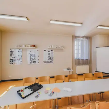 Ein heller Seminarraum mit großen Fenstern, Tischen und Stühlen – ideal für Workshops, Gruppenarbeit und kreative Lernphasen.