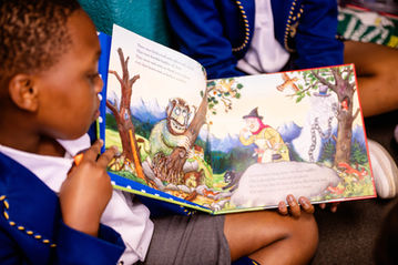 An image of a Grade 7 learner reading to a Grade 1 learner in class.