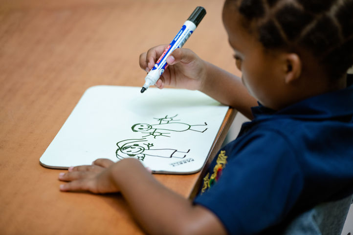Grade 1 child developing writing skills using a whiteboard and marker.