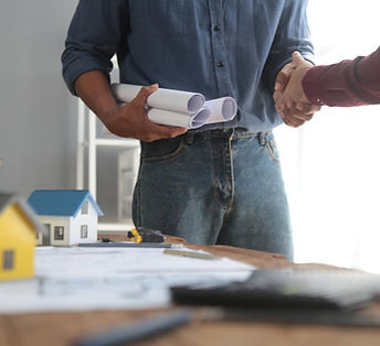 two professionals shaking hands over architectural plans and model homes
