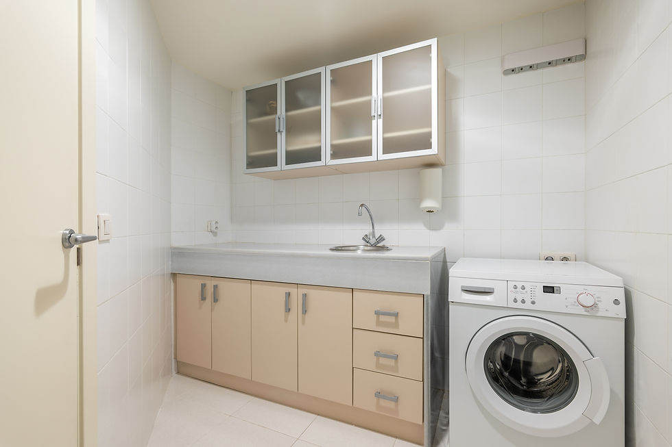 A small laundry room with a washing machine, a sink, and storage cabinets