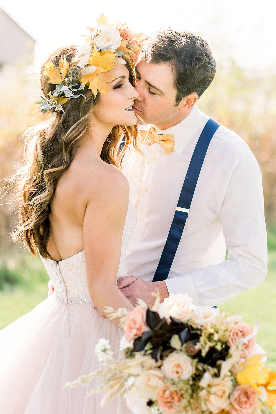 autumn bride wearing flower crown and groom kiss in a grass field