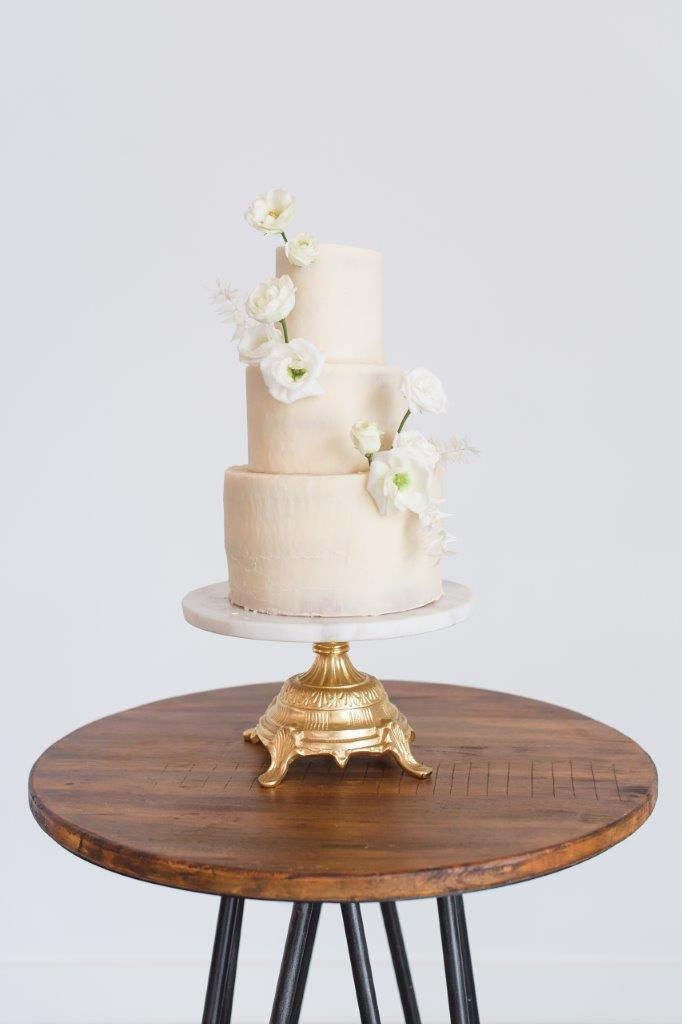 Minimalist ivory wedding cake on gold and marble stand with white lisianthus flowers