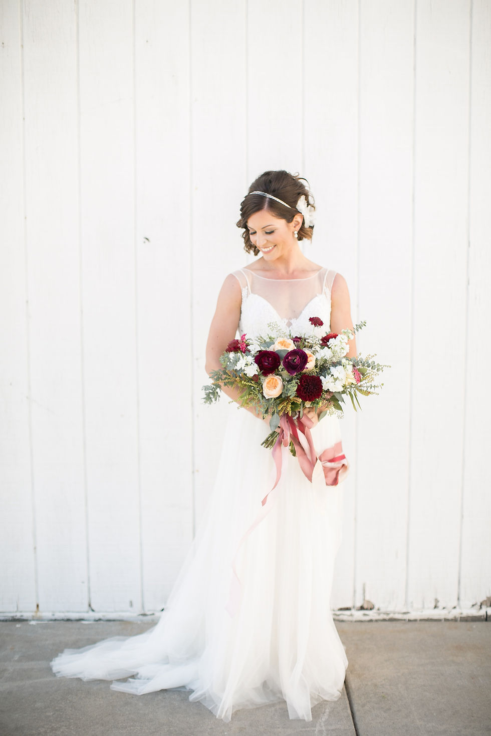 bride holding wedding bouquet by studio bloom iowa of juliet roses, ranunculus, dahlias, and eucalyptus on white barn wall