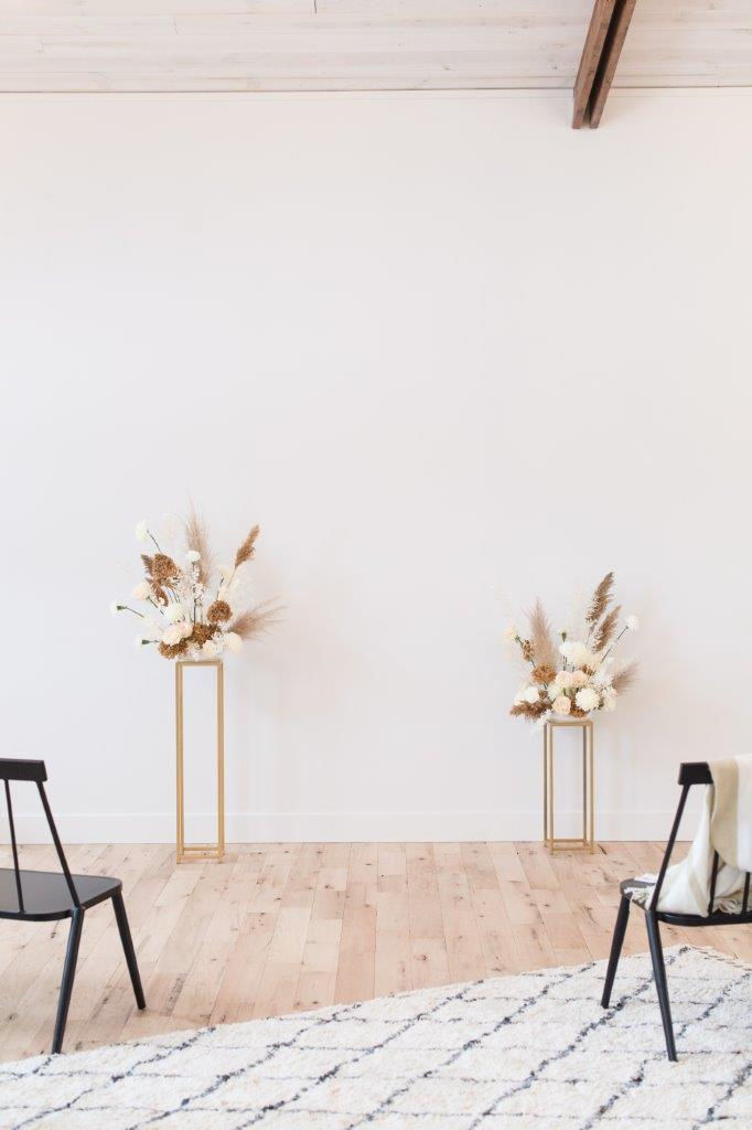 Minimalist wedding ceremony flowers by Studio Bloom Iowa in white and tan on gold stands with roses, pampas, and carnations