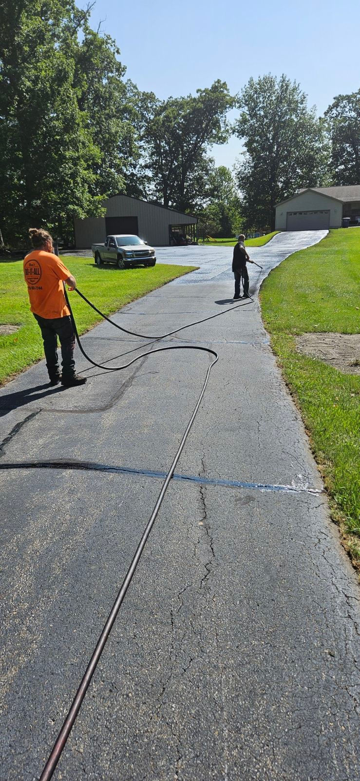 Freshly sealcoated residential driveway in Michigan City with crews applying crack seal and a clean top coat before winter.