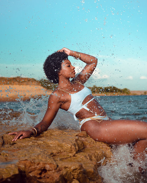 Swimsuit model in photoshoot on lake with waves crashing on the shore