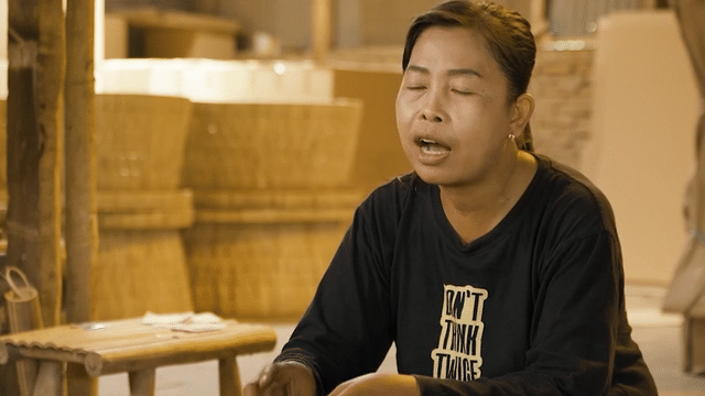 A woman in a black shirt is sitting on a wooden stool with her eyes closed for a video production agency.