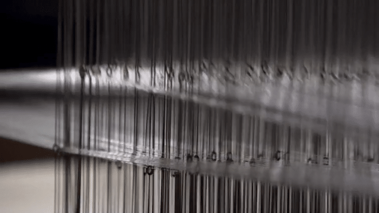 The media displays close-up camera angles of the loom in production. The strings of the textile mill loom intersect the fabrics and then the looped media cuts finally to the fabric string rolls releasing the fabric giving the viewer a sense of how furniture manufacture takes place.