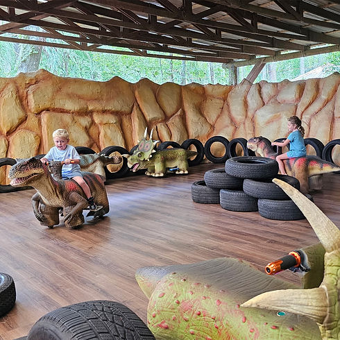 Children riding on mechanical dinosaurs with stacks of tires nearby