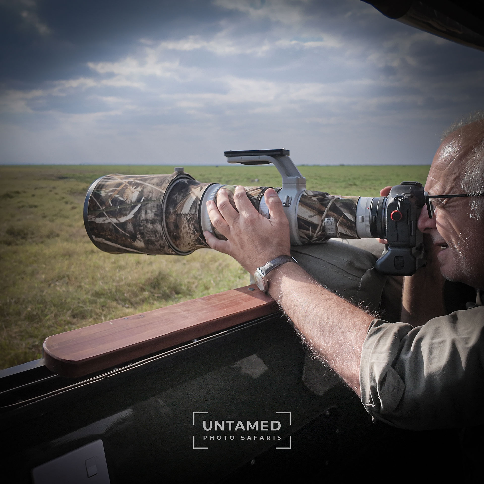 Wildlife photographer with a telephoto lens takes photographs during a photographic safari in the Masai Mara.