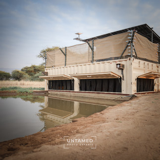 A photographic safari hide known as Shompole Plains hide next to a waterhole with its doors open during the day used during Untamed Photo Safaris
