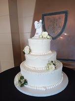 Three tiers of vegan vanilla cake decorated in a monochrome white palette of delicate piping, fresh flowers, and a customer-provided ceramic topper.