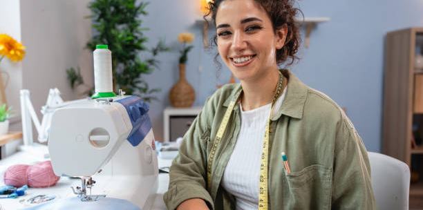 imgi_53_a-young-designer-works-with-a-smile-at-her-workplace-next-to-a-sewing-machine.png