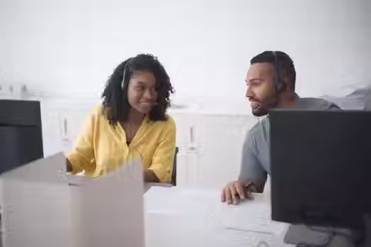 IT support professional assisting a client at a desk with computer monitors in a modern office.